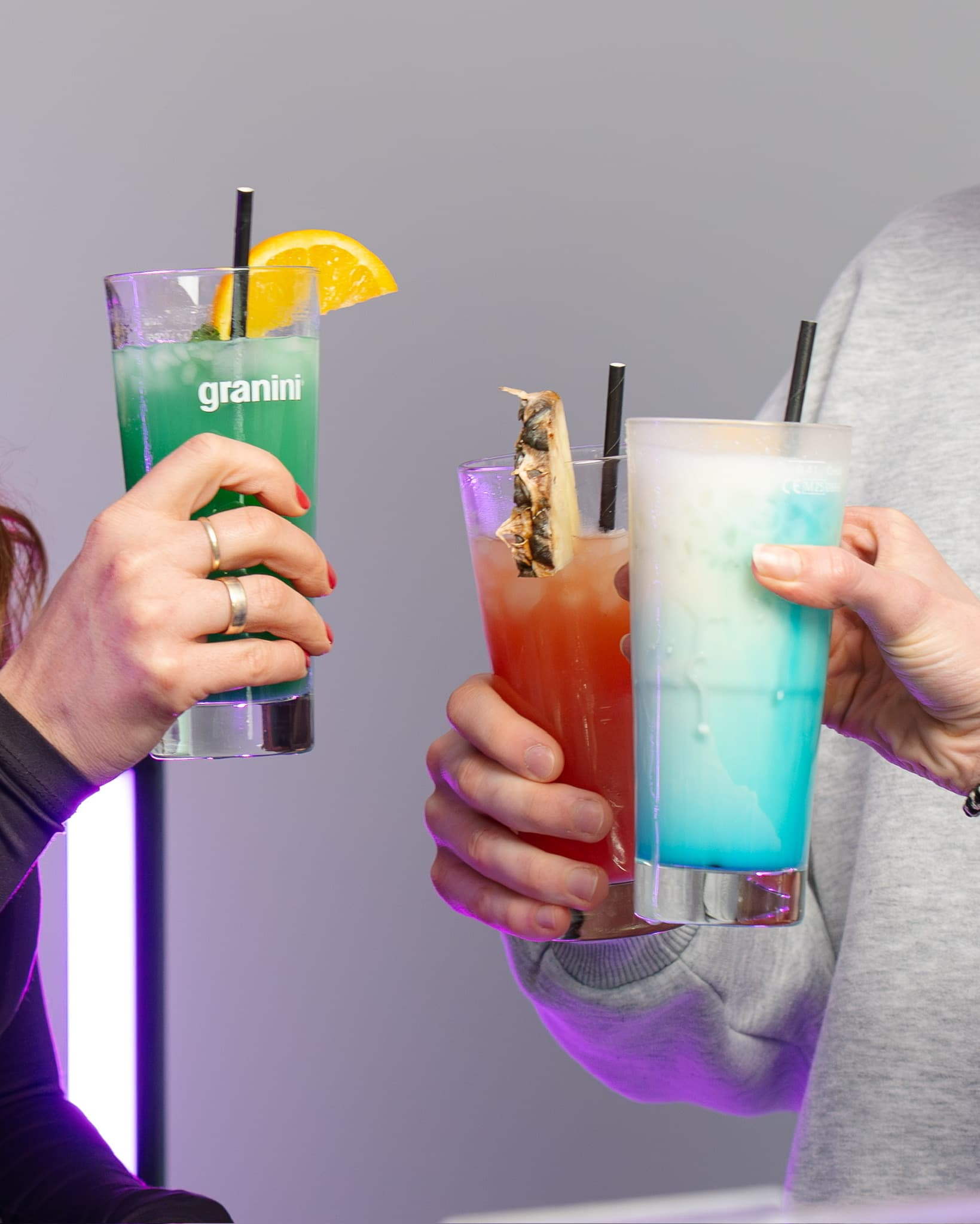 Drei Gäste halten farbige Cocktails in der Hand